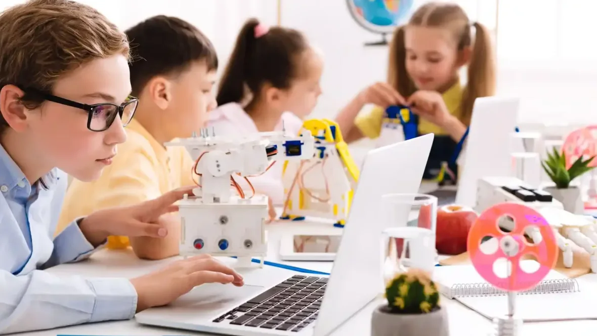 Dzieci pracują przy komputerach i budują roboty podczas zajęć technologicznych